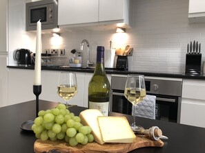 A kitchen counter with a bottle of wine, two glasses of wine, a candle, a bunch of grapes, and a piece of cheese. - Cosy One Bedroom Apartment By Creatick (Reading)