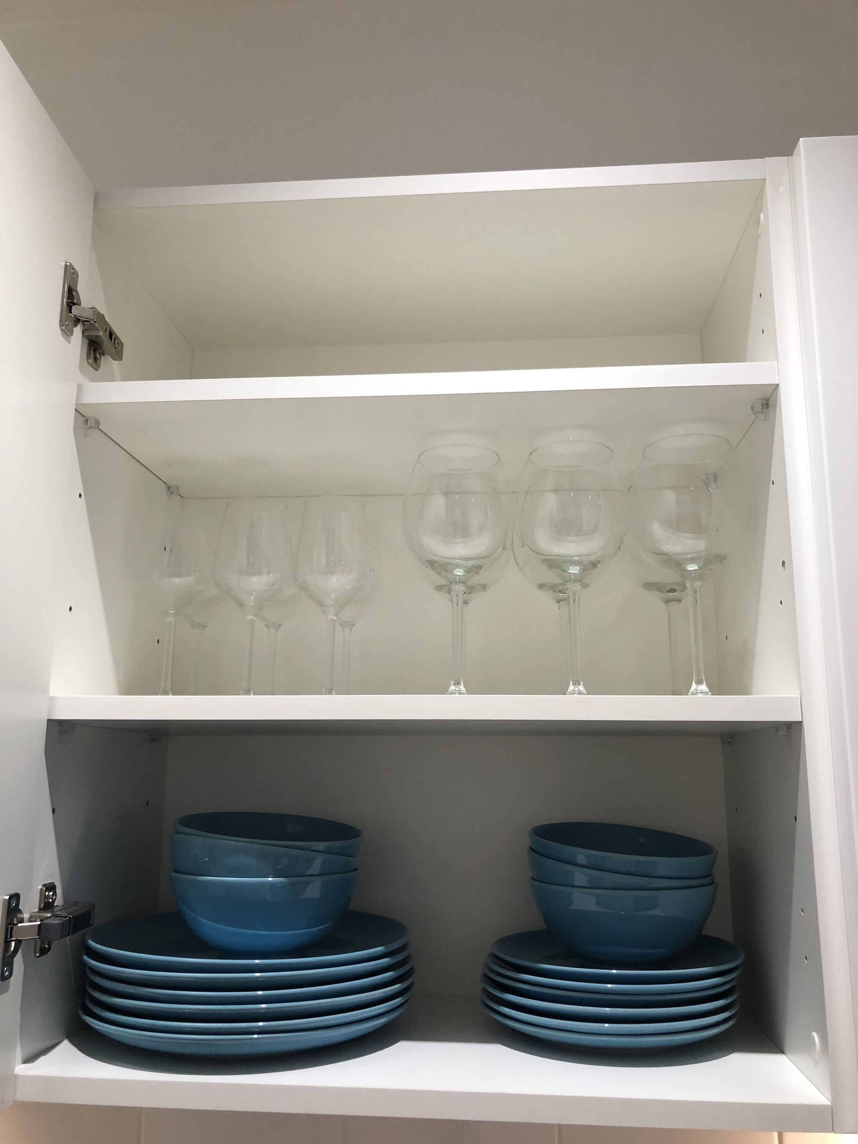 A white cabinet with shelves containing blue bowls and wine glasses.