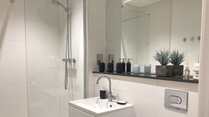 A modern bathroom with a glass shower enclosure, a white sink with a black soap dispenser, and a mirror above the sink. - Cosy One Bedroom Apartment By Creatick (Reading)