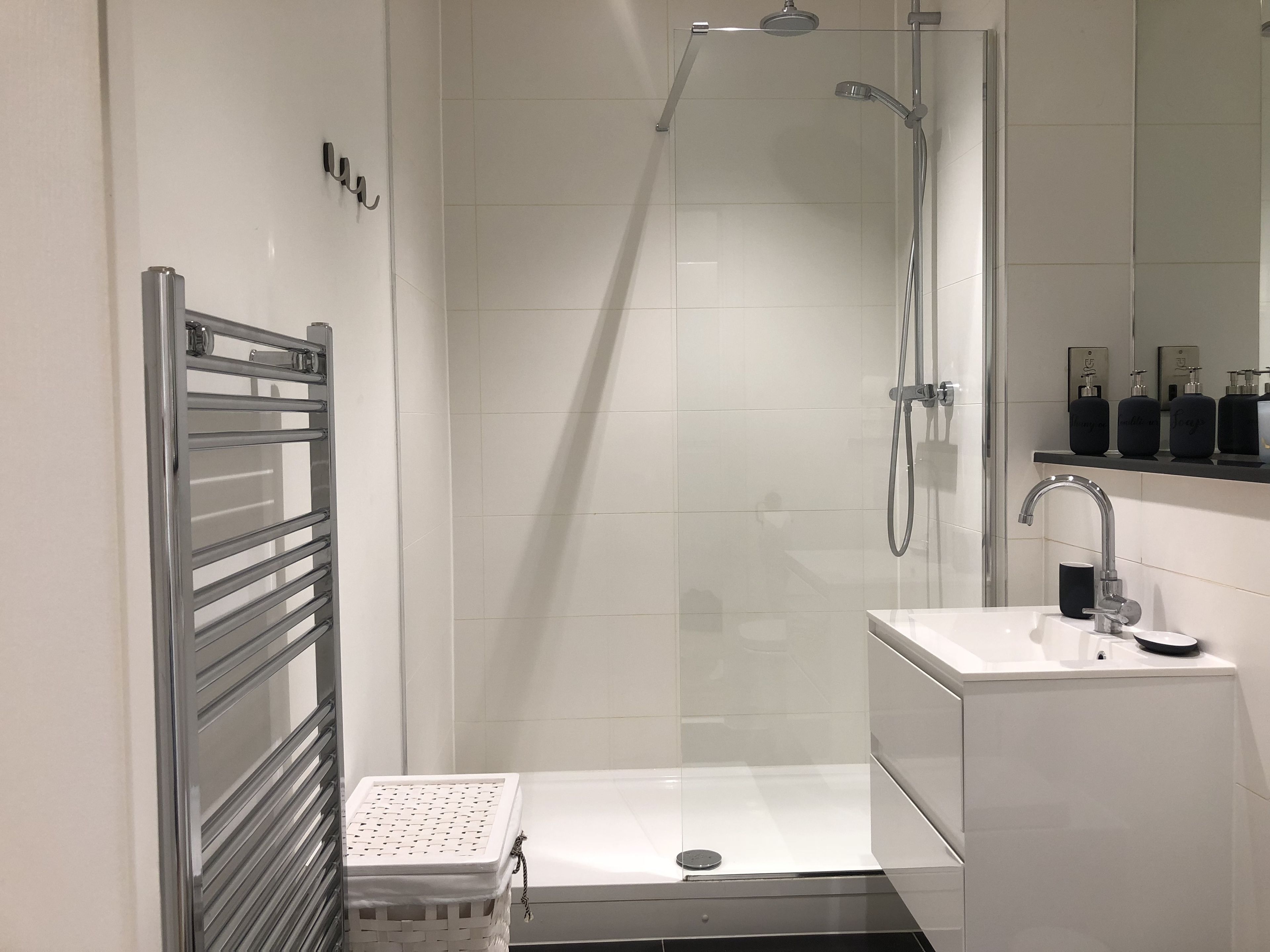 A modern bathroom with a glass-enclosed shower, a white sink, and a towel rack.