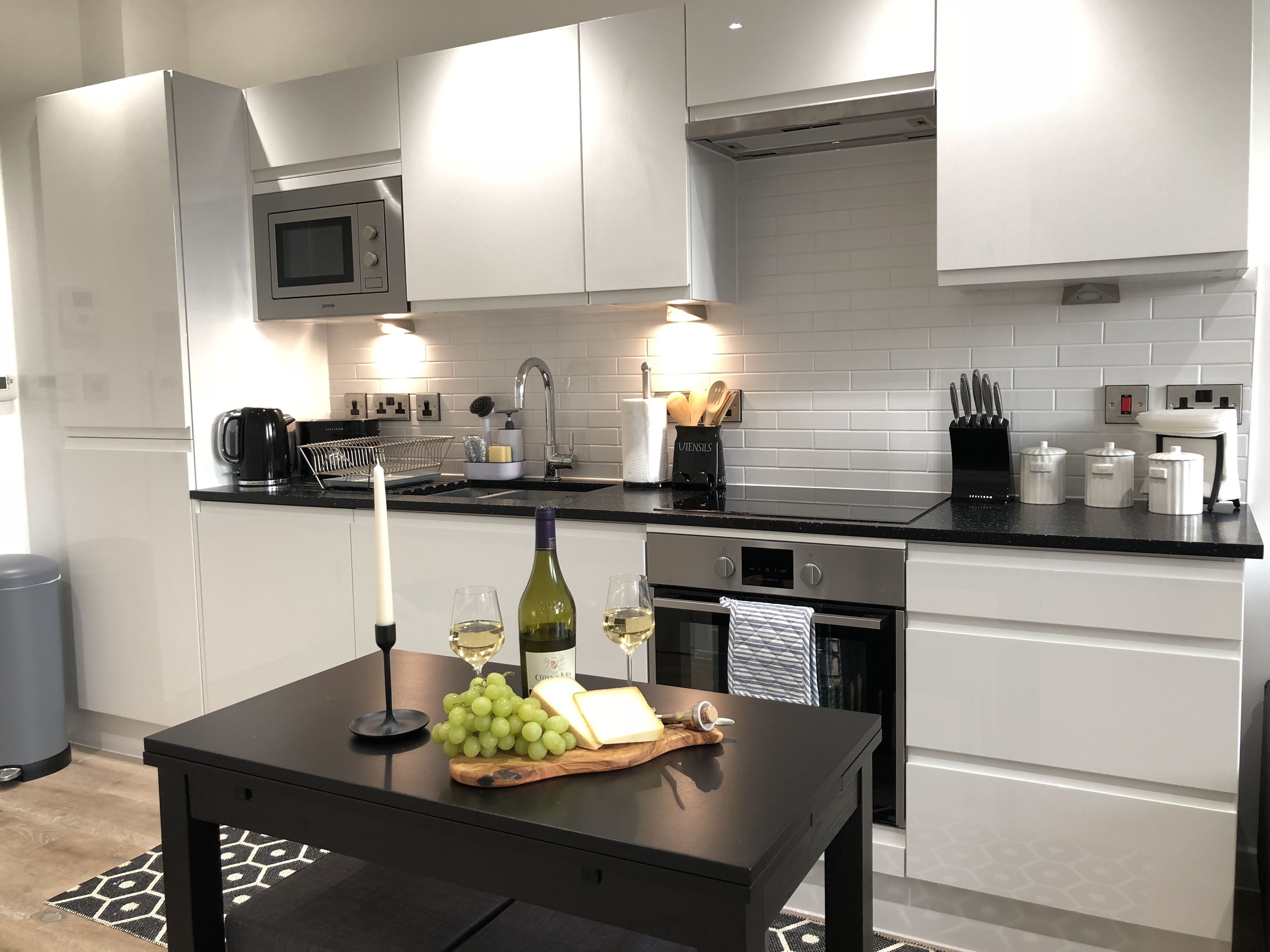 A modern kitchen with white cabinets, a black countertop, a stainless steel microwave, and a built-in oven.