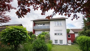 Ein zweistöckiges Wohngebäude mit Balkon im oberen Geschoss, umgeben von Grünflächen und einem gepflegten Rasen.