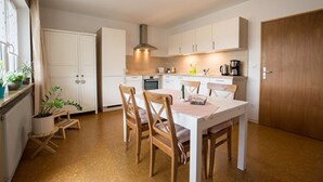 Eine moderne Küche mit weißen Schränken, einem Holztisch und Stühlen. Auf der Arbeitsplatte steht eine Kaffeemaschine.