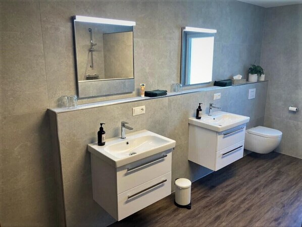 A modern bathroom with two sinks, a toilet, and a mirror above each sink.