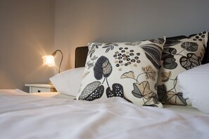 Una cama bien hecha con ropa blanca y almohadas estampadas.