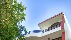 A multi-story building with a curved facade, balconies with red railings, and a visible water spigot. - The Desire Hostel (New Delhi)