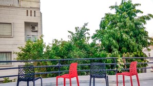 Outdoor seating with metal chairs and a railing, surrounded by greenery and a building. - The Desire Hostel (New Delhi)