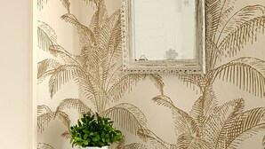 Une pièce avec un papier peint à motifs, une commode avec des tiroirs et une plante en pot.