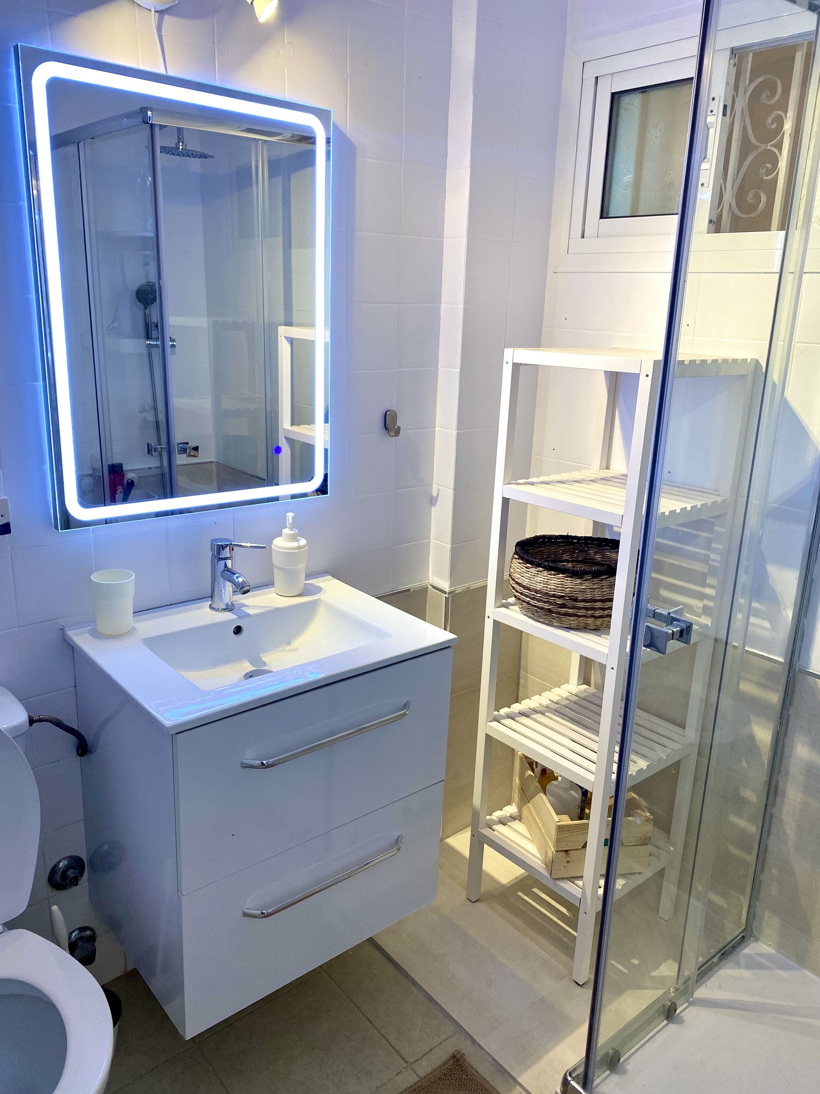 Une salle de bain moderne dotée d’une douche à parois de verre, d’un meuble-lavabo blanc avec un miroir et d’une étagère intégrée.