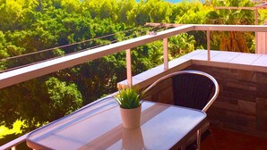 Un balcon avec une table et des chaises, un pot de fleurs et une vue sur l’océan et la végétation.