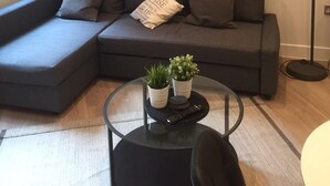 A modern living room with a sectional sofa, a round coffee table with plants, a floor lamp, and a painting on the wall. - Modern Apartment By Creatick (Reading)