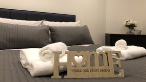 A neatly made bed with grey bedding, a framed picture on the wall, and a 'Home' sign on the bed. - Modern Apartment By Creatick (Reading)