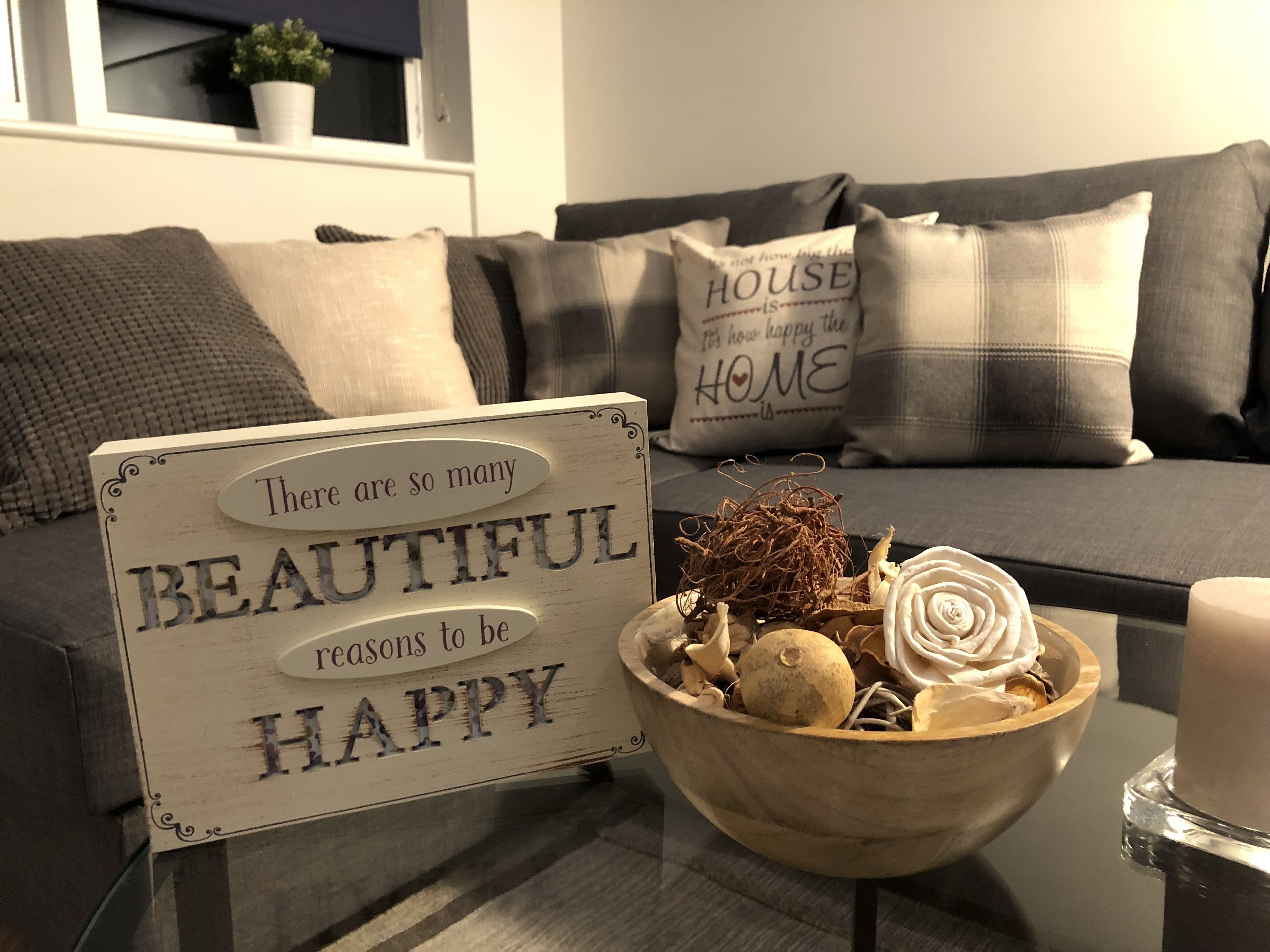 A cozy living room with a sign that reads "There are so many BEAUTIFUL reasons to be HAPPY" and a wooden bowl with decorative items on a coffee table.