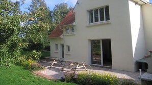 A white two-story house with a red-tiled roof, a patio with a picnic table, and a garden with yellow flowers. - Gite in France, 3 stars, 11 prs, comfortable, relaxing, in natural environment (Vacqueriette-Erquières)