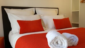 A neatly made bed with white and red bedding, a black headboard, and a white towel on the bed. - Gîtes Les COSTANS & A Proximité plages 800M & Commerces 300M (Perros-Guirec)