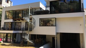 A modern two-story building with a spiral staircase, large windows, and outdoor seating. - Gîtes Les COSTANS & A Proximité plages 800M & Commerces 300M (Perros-Guirec)