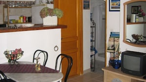 Ein Essbereich mit einem runden Tisch, schwarzen Stühlen, einem Holzschrank mit Fernseher und einer Küchenzeile mit Holztür und Regalen.
