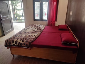 A single bed with a leopard print bedspread and red pillows in a room with a wooden floor and a window with red curtains. - International Youth Club - Hostel (Dharamshala)