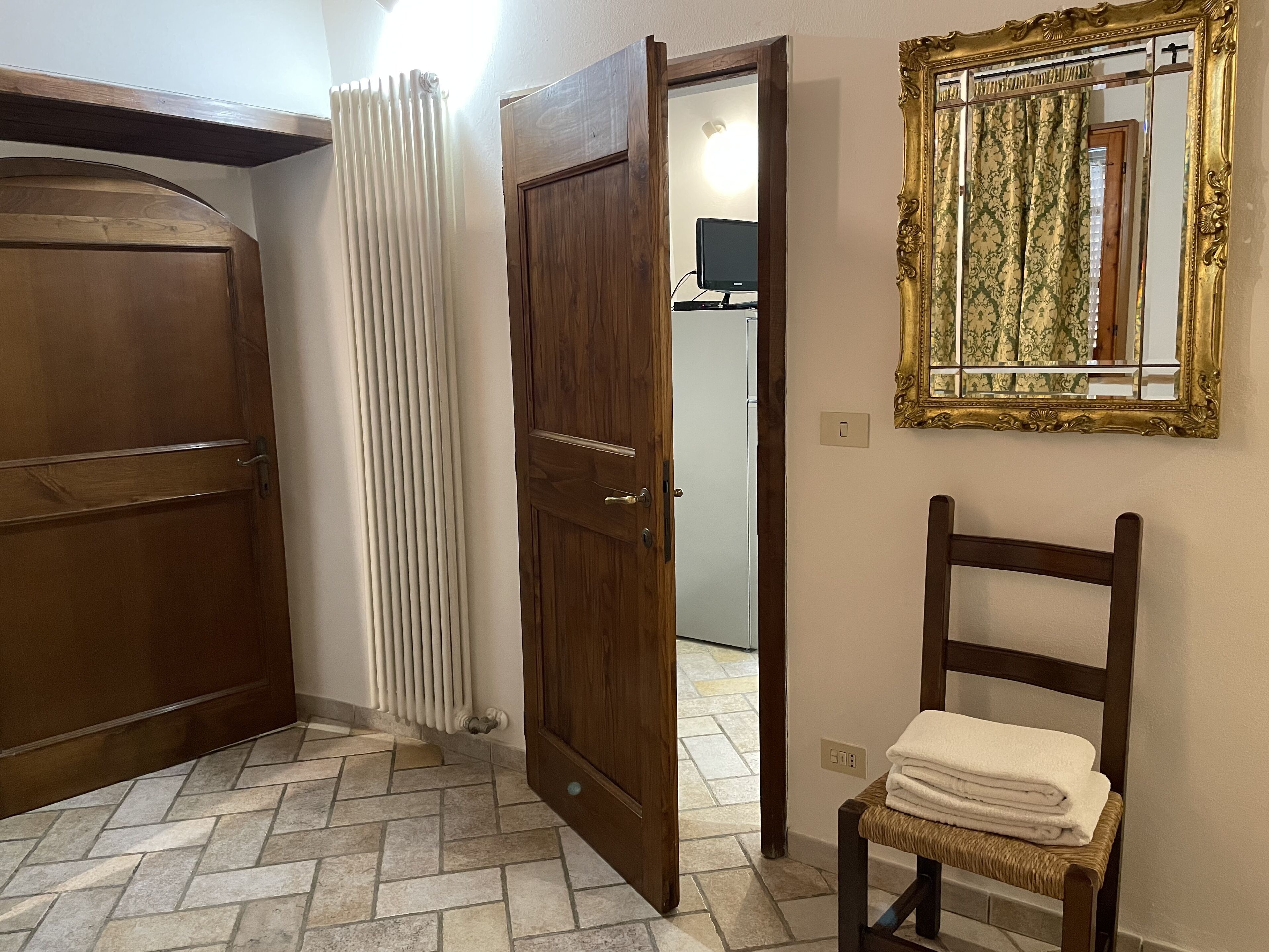 A room with a wooden door, a radiator, a chair with towels, and a mirror on the wall.