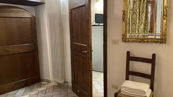 A room with a wooden door, a radiator, a chair with towels, and a mirror on the wall.