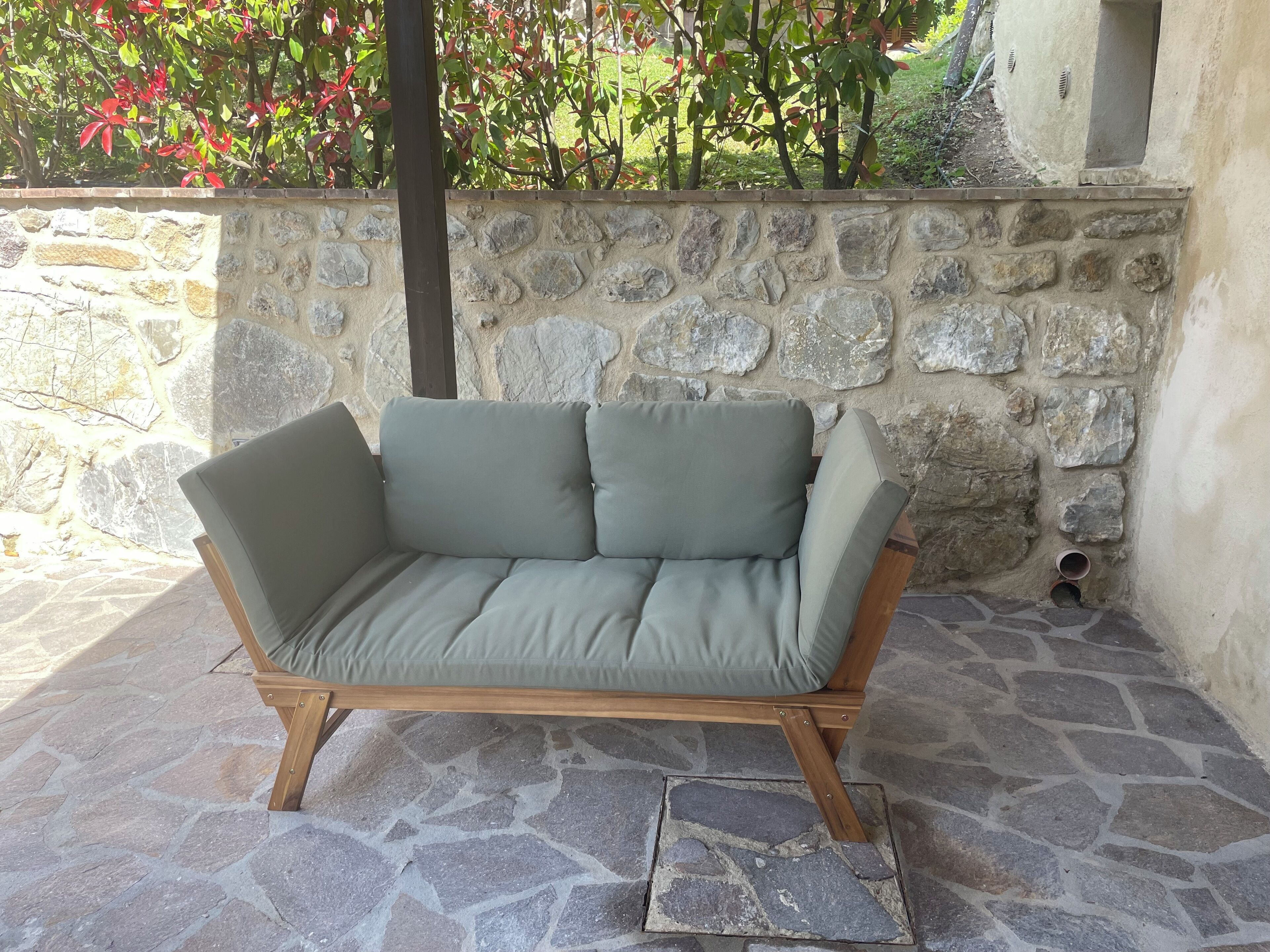 A stone-floored outdoor seating area with a stone wall and a wooden-framed sofa.