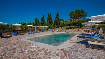 Zona de piscina amb paviment de pedra, gandules i ombrelles.