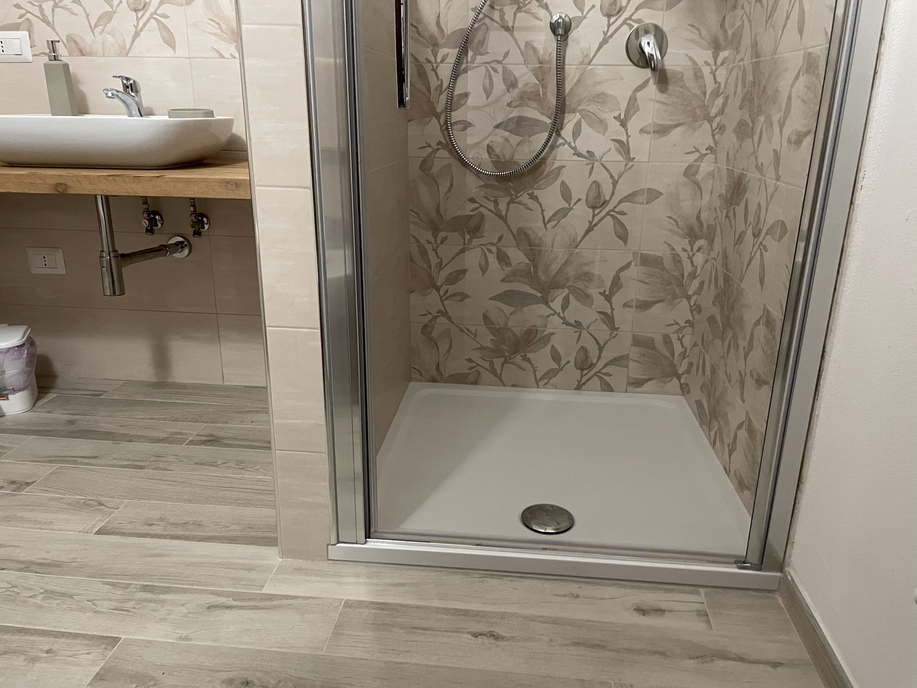 A shower with a glass door, a sink, and a wooden countertop in a bathroom.