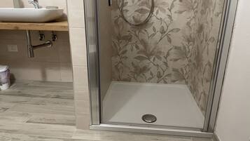 A shower with a glass door, a sink, and a wooden countertop in a bathroom.
