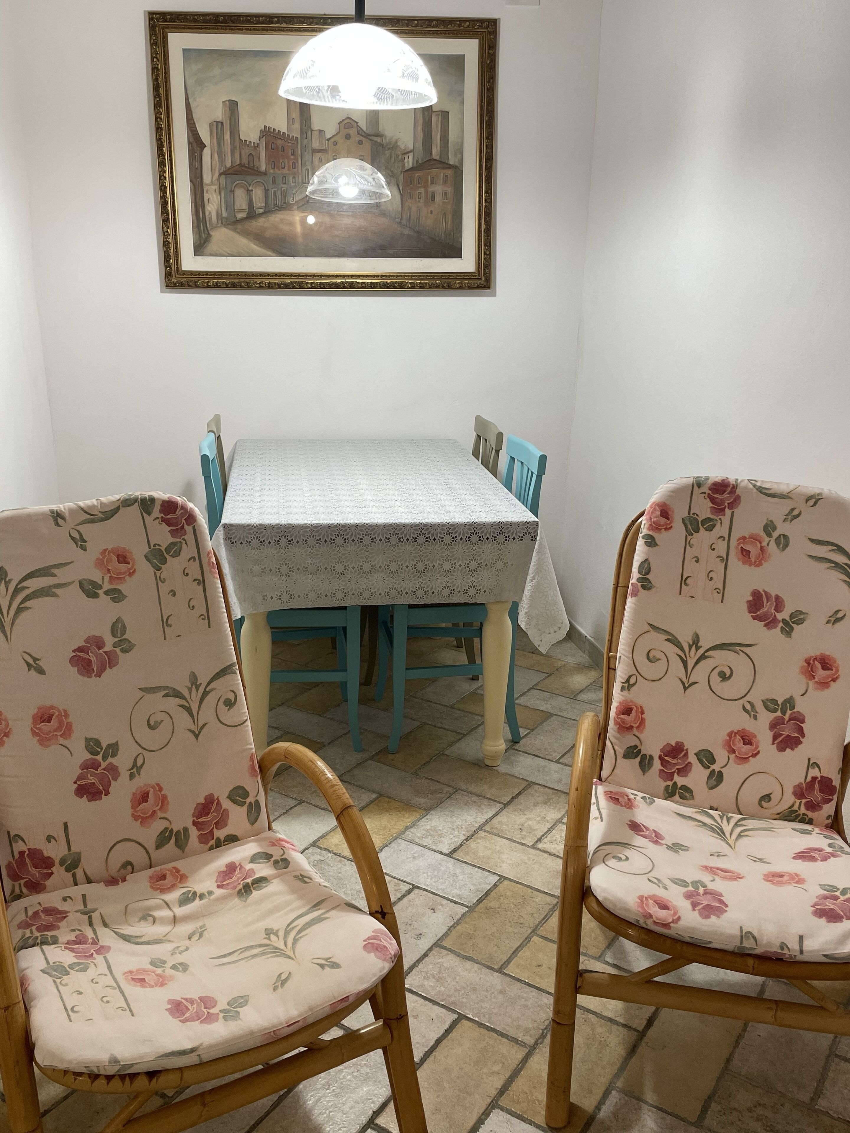 A dining area with a table and chairs, a framed painting above, and a tiled floor.