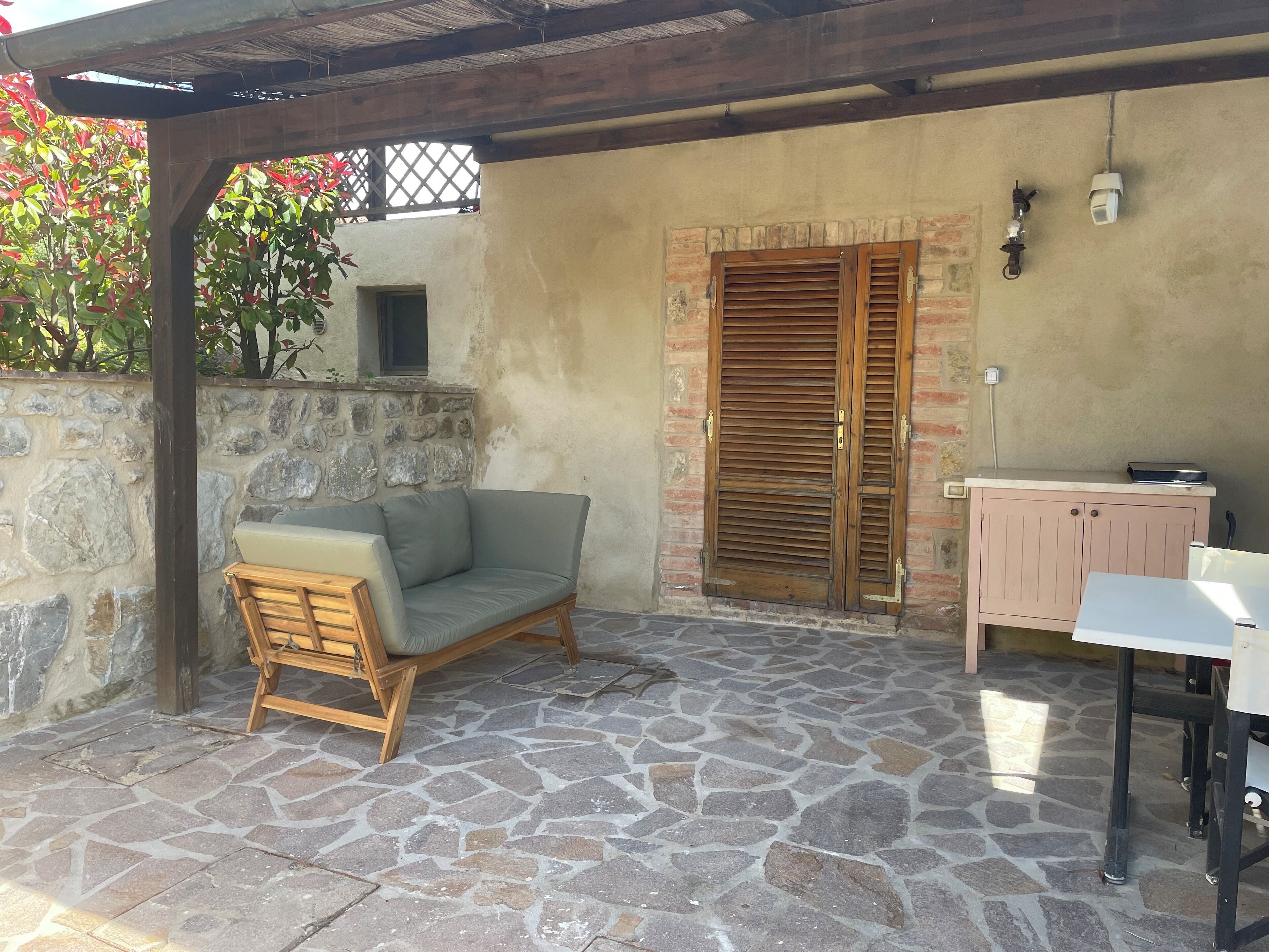 Un patio con suelo de piedra, un banco de madera y un sofá con cojines.
