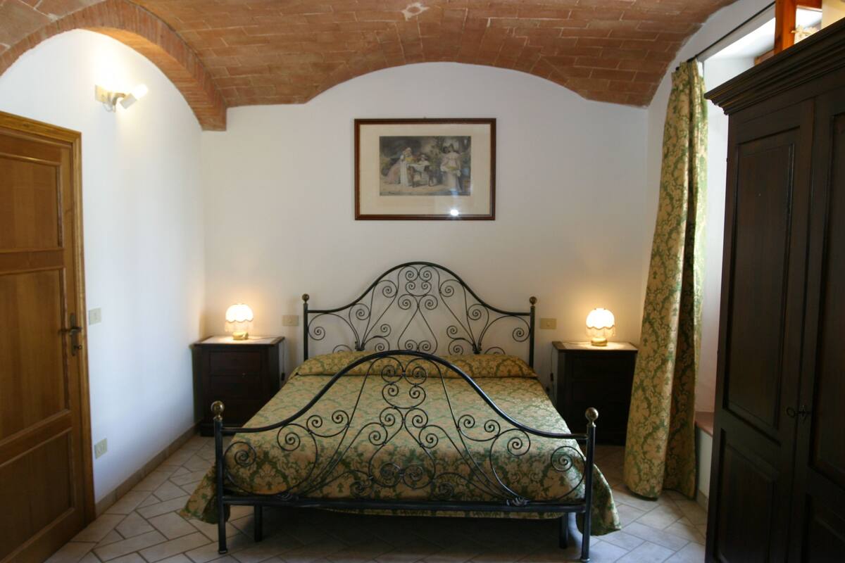 A bedroom with a bed, two bedside tables, a picture on the wall, and a wooden door.