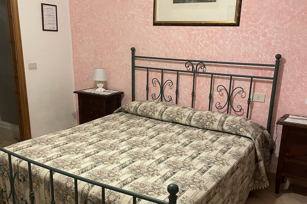 A bedroom with a bed, a nightstand, a framed picture on the wall, and a door.