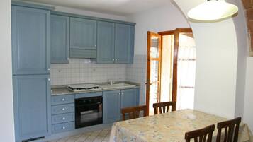 Una cocina con armarios azules, salpicadero de azulejos, un lavamanos y una zona de comedor con una mesa y sillas.