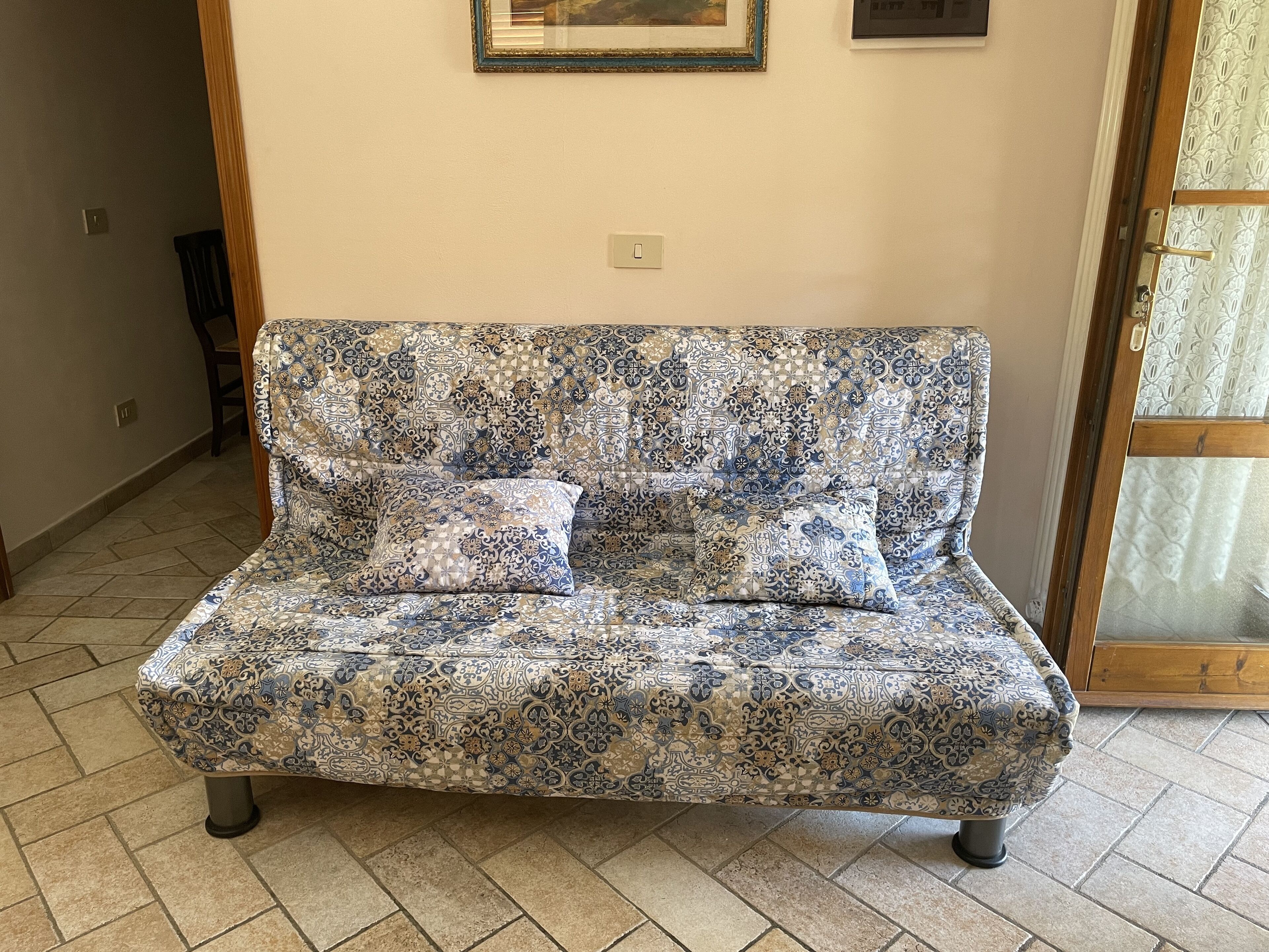A patterned sofa with two cushions in a room with tiled flooring and a door with a glass panel.