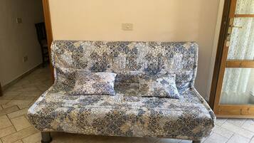 A patterned sofa with two cushions in a room with tiled flooring and a door with a glass panel.