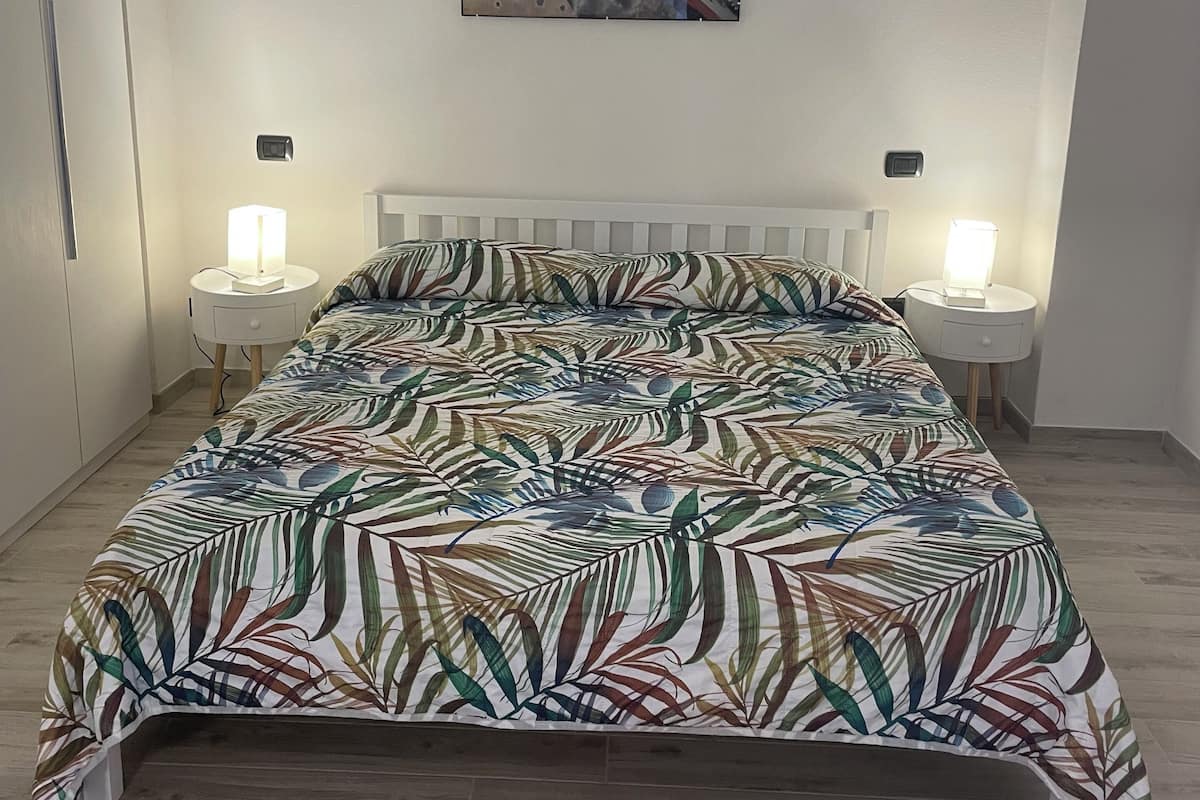A bedroom with a bed, two bedside tables, a wall-mounted artwork, and a white headboard.