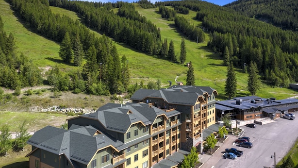 A multi-story hotel with a ski resort view, featuring a parking lot and a mountainous backdrop. - Incredible ski and summer condo!! Direct ski in and out, hot tub , gym, covered parking!! (Whitefish)
