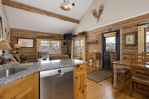 A rustic cabin interior with a kitchen, dining area, and living space. - Ski-in/Ski-out Cowboy Heaven Cabin - 360 Degree Mtn Views - Private Hot Tub (Big Sky)