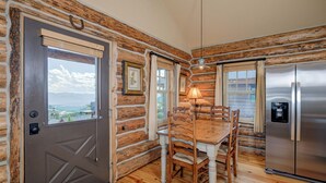A log cabin interior with a dining table, chairs, a refrigerator, and a door leading to a scenic view. - Ski-in/ski-out "Alpine Escape" Cowboy Heaven Cabin-360 Degree Mtn View - Hot Tub (Big Sky)