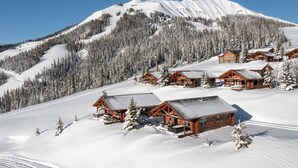 A snow-covered mountain with a clear sky. There are several wooden cabins with sloped roofs, surrounded by snow-laden trees. - Ski-in/ski-out "Alpine Escape" Cowboy Heaven Cabin-360 Degree Mtn View - Hot Tub (Big Sky)