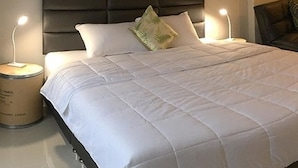 A neatly made bed with a white duvet, two bedside lamps, and a dark headboard. - Splash (Bangkok)