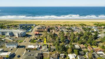 An aerial view of a coastal residential area with houses, a parking lot, and a beach in the background.