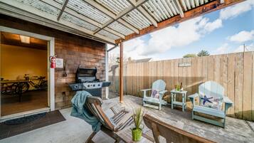 An outdoor patio with a grill, seating, and a wooden fence.