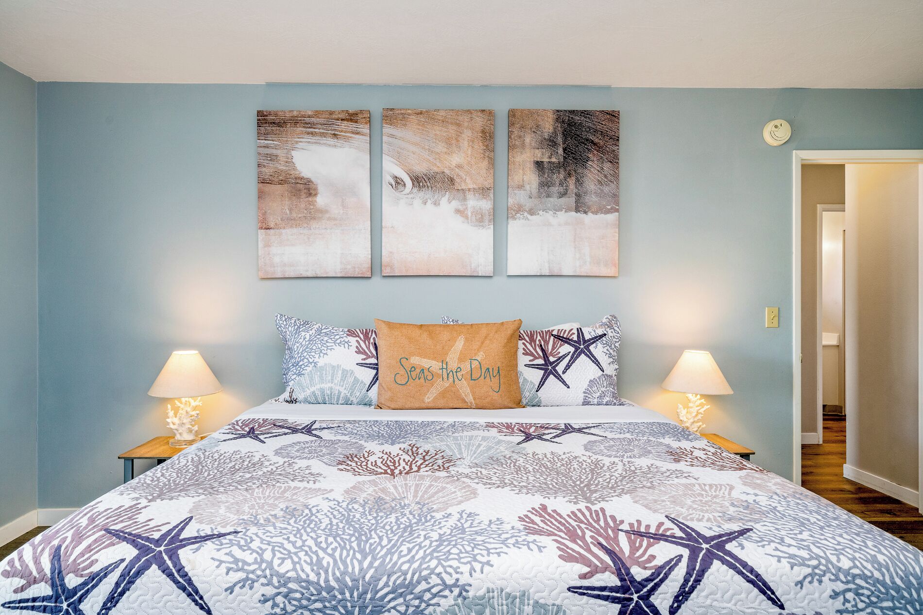 A bedroom with a bed, two nightstands, and three wall art pieces.