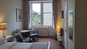 A bedroom with a bed, a desk, a chair, a radiator, and a window with curtains.