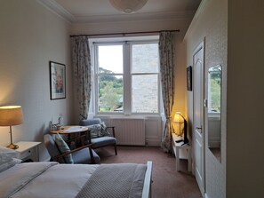A bedroom with a bed, a desk, a chair, a radiator, and a window with curtains.