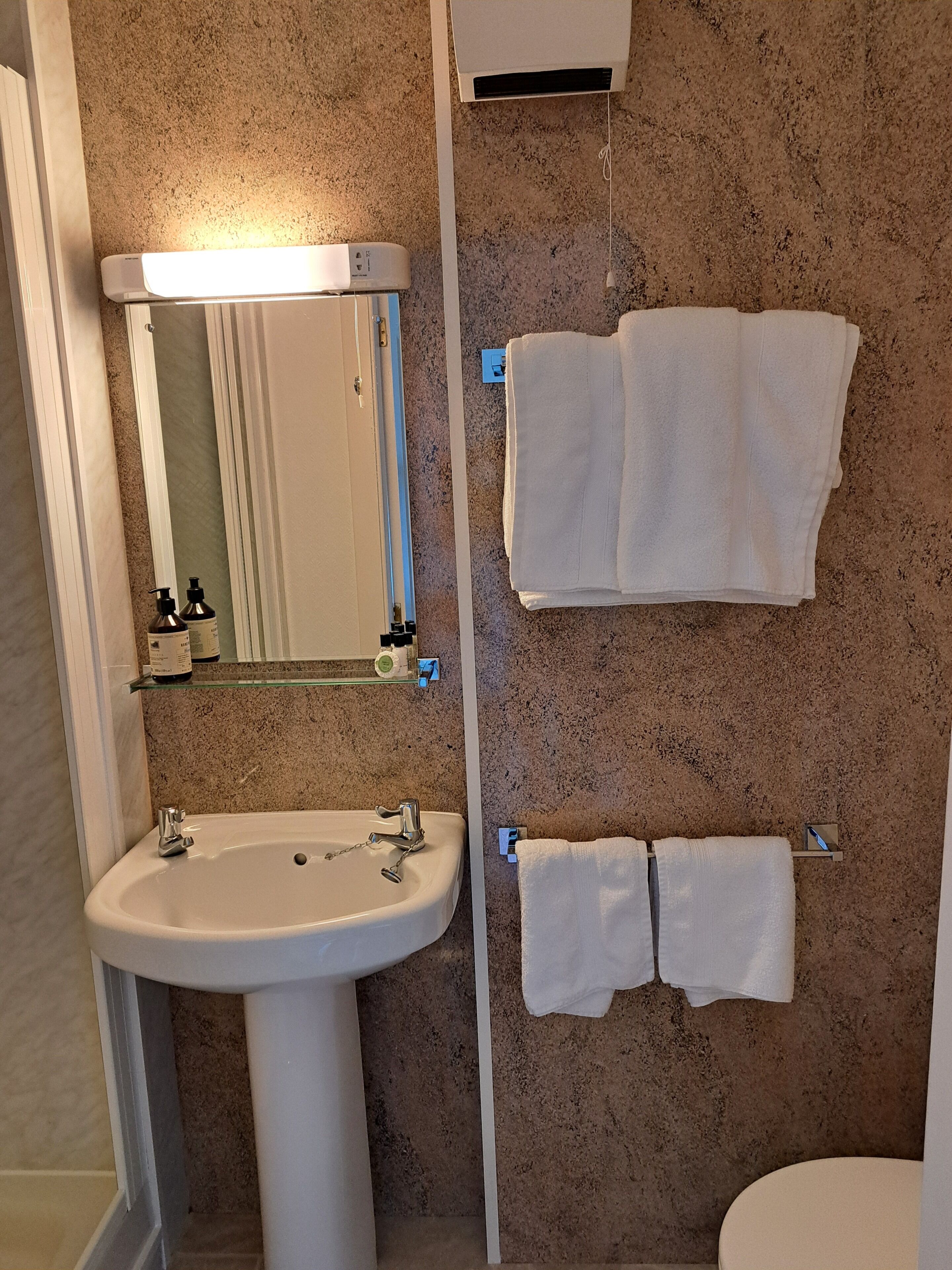 Ein Badezimmer mit einem Standwaschbecken, einem Spiegel, zwei weißen Handtüchern und einem Handtuchhalter.