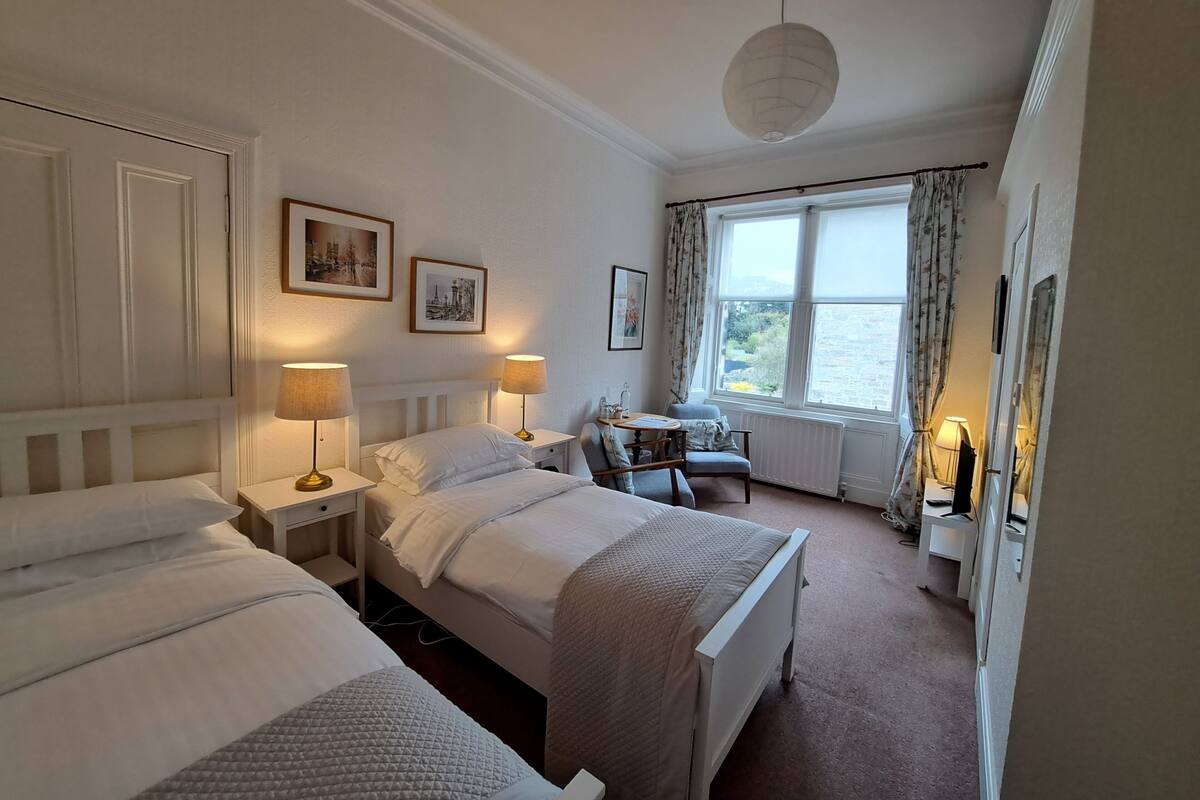 A hotel room with two beds, a desk, a chair, and a view of the outdoors.