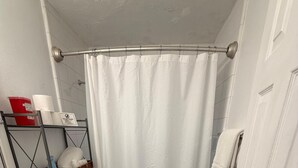 Ein kleines Badezimmer mit Toilette, Duschvorhang, Ablagefläche für Pflegeprodukte und einer Tür.