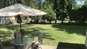 A patio with a round table and chairs, an umbrella, and a lawn.